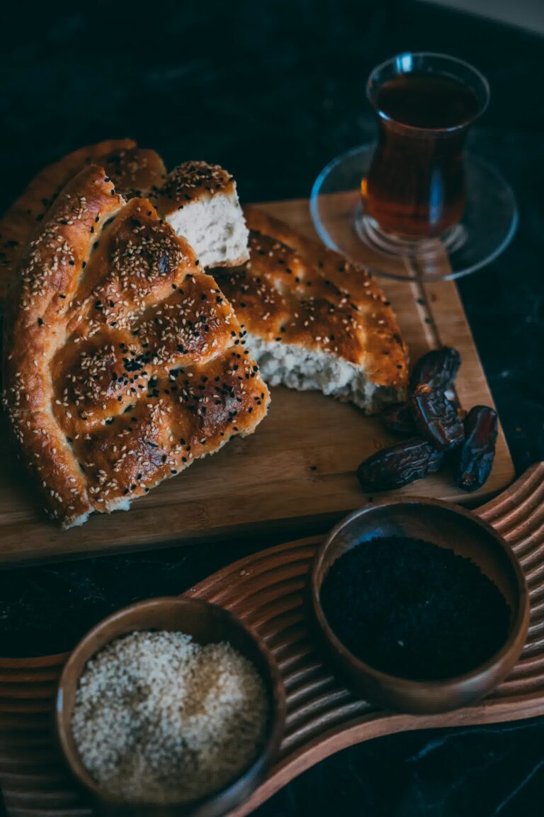 Miche De Pain Fraîchement Cuit, Recouverte De Graines Noires De Nigelle, Accompagnée D'Un Bol D'Huile De Nigelle Habachia Et De Dattes Fraîches.